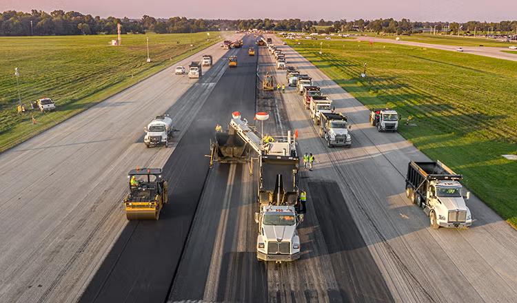 Large paving crew and equipment convoy handling a heavy-load airport runway paving project