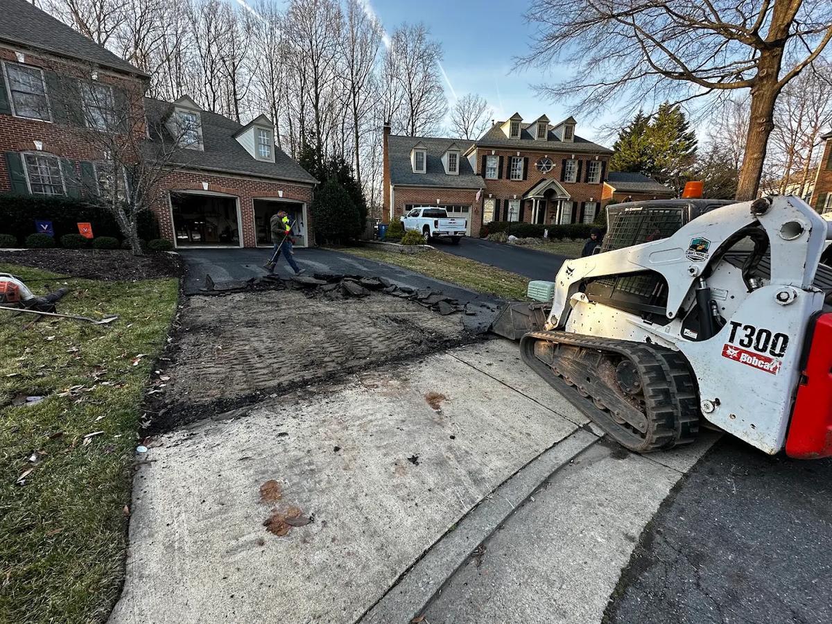 Asphalt removal in progress on a residential driveway in Northern Virginia — a skid steer tearing out the old asphalt surface