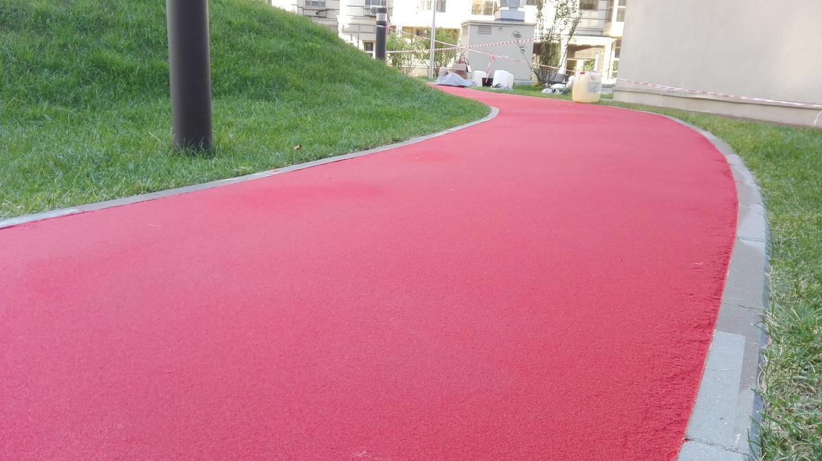 Colored pavement path finished in a vivid red tone, curving through a landscaped area