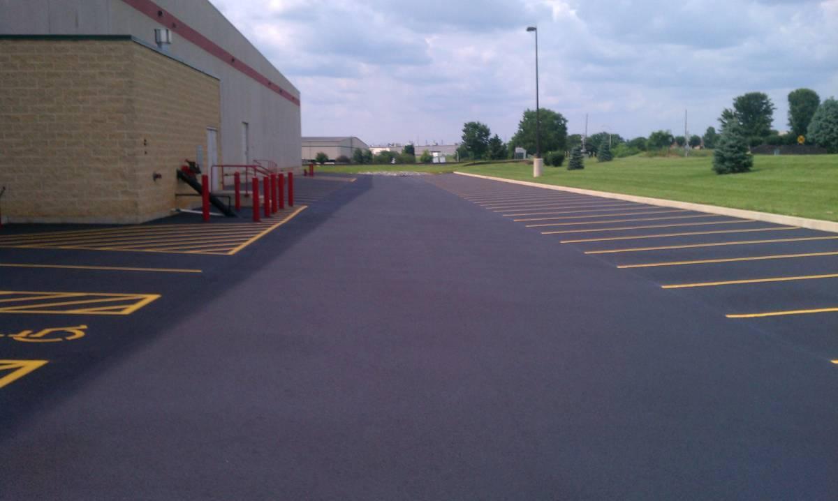 Commercial sealcoating completed on a business parking lot, finished with crisp yellow striping