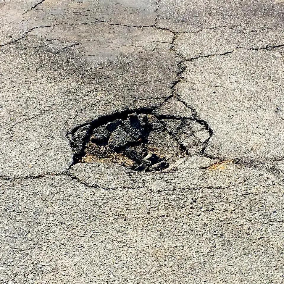Emergency pothole repair needed — a deep, jagged pothole breaking through an asphalt surface in Northern Virginia