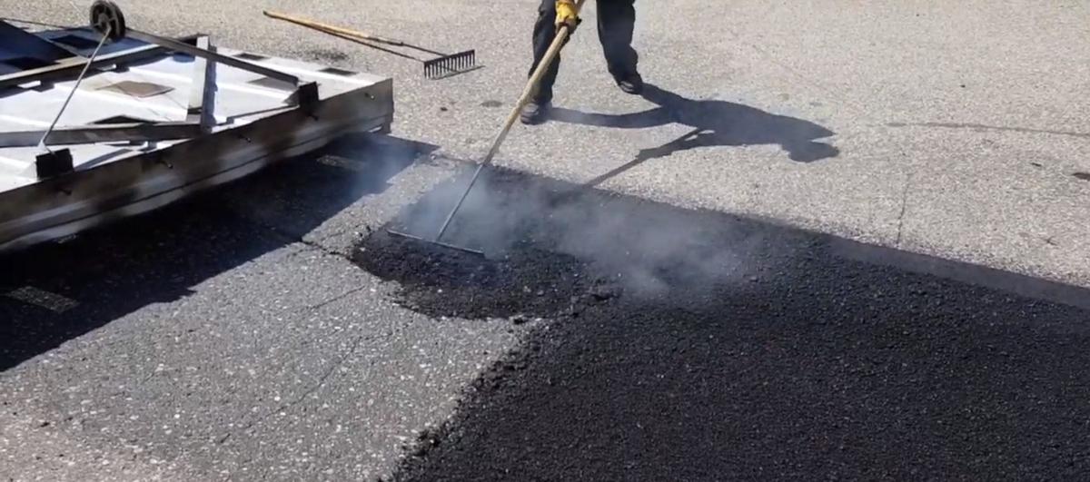Infrared asphalt repair in progress — a heating panel softens the existing asphalt so it can be raked and blended seamlessly with the new patch