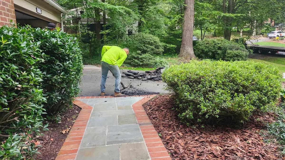 Crew working to remove an asphalt driveway by hand near a home's walkway in Northern Virginia