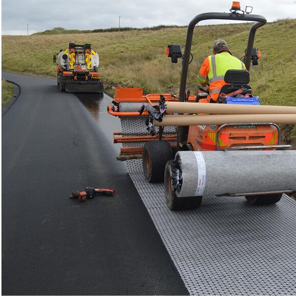 Road construction company at work — a crew laying reinforcement fabric ahead of paving on a rural road