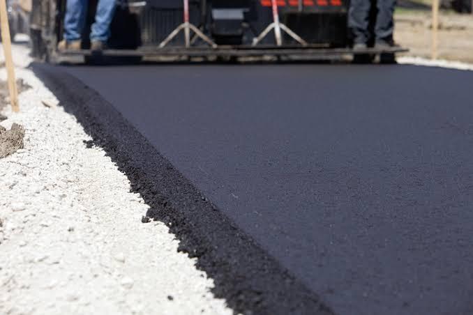 Road installation in progress — a paver machine laying fresh asphalt along the edge of a new road