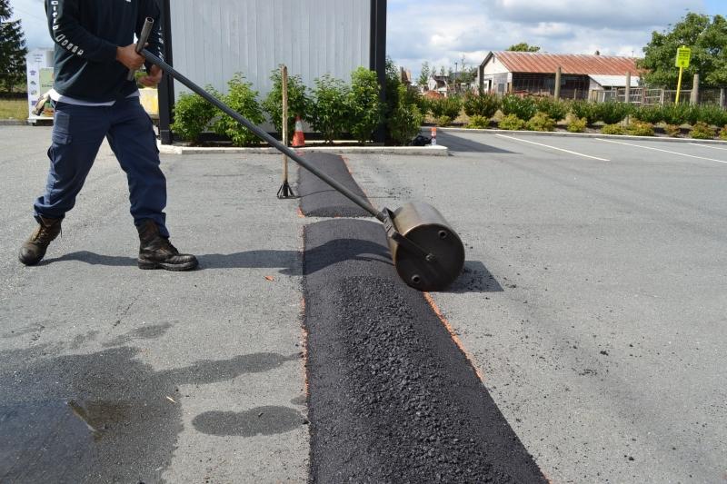 Speed bump installation in progress — a worker using a hand roller to shape a fresh asphalt speed bump in a parking lot